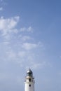 Tip of a white lighthouse with a weather vane on the roof, a blue sky in the background with some clouds, copy space Royalty Free Stock Photo