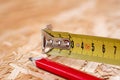 A tip of yellow metal tape measure and red carpenter pencil lying on chip board. Blurred background Royalty Free Stock Photo