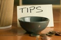 Tipping bowl in coffee shop with coins and coffee cup