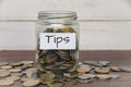 Tips label on coin jar on top of wooden desk with asorted coins background. Royalty Free Stock Photo