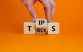 Tips and tricks symbol. Businessman turn the wooden cube and changes the word `tips` on `tricks`. Beautiful orange background.
