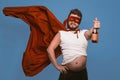 Tipsy superhero or antihero holds bottle of wine, man in superhero red mask with flying cloak holding bottle of alcohol