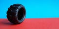 Tire on a red-blue double background. Close up toy black thick tyre with pattern. Side view. Place for copy space. Horizontal Royalty Free Stock Photo