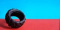 Tire on a red-blue double background. Close up toy black thick tyre with pattern. Side view. Place for copy space. Horizontal Royalty Free Stock Photo