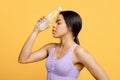 Tired african american sports woman with closed eyes holding bottle of water on her forehead, yellow background Royalty Free Stock Photo