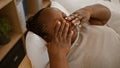 Tired african american woman, comfortably nestled in a relaxed bedroom setting, rubbing her eyes while lying on bed, waking up to Royalty Free Stock Photo