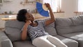 Black woman suffering from heatstroke flat without air-conditioner waving fan lying on couch at home