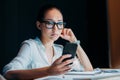 Tired asian businesswoman in eyeglasses using smartphone and working till late in office Royalty Free Stock Photo