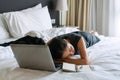Tired Asian businesswoman working on laptop computer in bed at hotel. Business trip, people and technology, overworked concept Royalty Free Stock Photo