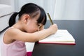 Tired Asian Chinese little girl writing on exercise book