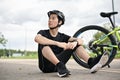 A tired Asian male cyclist in sportswear and a bike helmet sits on the street with his bike Royalty Free Stock Photo