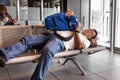 Tired Asian man sleeping flat on airport departure waiting area chairs while waiting for flight