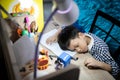 Tired asian student kid boy is sleeping with his head on a table while learning,problems of children asleep while studying online, Royalty Free Stock Photo