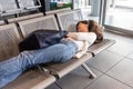 Tired Asian woman lie down sleeping flat on airport departure waiting area chairs while waiting for flight Royalty Free Stock Photo