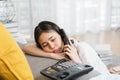 Tired Asian woman use phone and drowsy due to work on holidays. Royalty Free Stock Photo