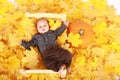 Tired baby boy lying on wooden bed in leaves by pumpkin - Halloween Royalty Free Stock Photo