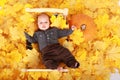 Tired baby boy lying on wooden bed in leaves by pumpkin - Halloween Royalty Free Stock Photo