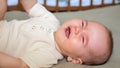 Tired baby girl cries lying on brown bed in empty nursery Royalty Free Stock Photo