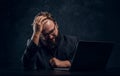 Tired bearded programmer sitting at the table with laptop in office