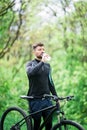 Tired biker resting and drinking from water bottle in green park