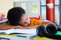 Tired biracial schoolboy sitting at desk and lying on books in classroom Royalty Free Stock Photo