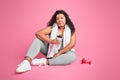 Tired black body positive woman in sportswear sitting on floor, holding bottle of water, have break after workout Royalty Free Stock Photo