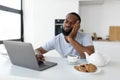Tired black man using laptop sitting at kitchen table Royalty Free Stock Photo