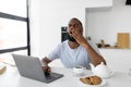 Tired black man yawning using laptop sitting at kitchen table Royalty Free Stock Photo