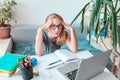 Tired and bored beautiful young school girl left-handed working at home in her room with a laptop and class notes studying in a