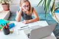 Tired and bored beautiful young school girl left-handed working at home in her room with a laptop and class notes studying in a