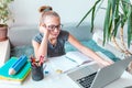 Tired and bored beautiful young school girl left-handed working at home in her room with a laptop and class notes studying in a