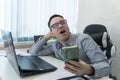 Tired bored businessman yawning at workplace near laptop, looking smartphone, checking time, boring work, dead end job Royalty Free Stock Photo