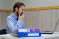 Tired bored young businessman sitting at his desk in front of his computer yawning Royalty Free Stock Photo