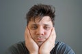 Tired boring shaggy young man is looking at camera on grey background.