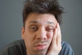 Tired boring shaggy young man is looking at camera on grey background.