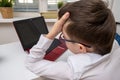 A tired boy, schoolboy in white formal shirt sitting by the table, desk with laptop and doing homework at home, e-learning and Royalty Free Stock Photo