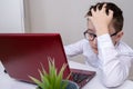 A tired boy, schoolboy in white formal shirt sitting by the table, desk with laptop and doing homework at home, e-learning and Royalty Free Stock Photo