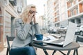 Tired business woman with laptop in outdoor cafe, woman touching her eyes with her glasses off, city street background Royalty Free Stock Photo