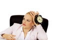 Tired business woman sitting behind the desk and holding alarm clock Royalty Free Stock Photo
