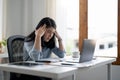 Tired business woman in stress works at a laptop while sitting at a table at home and holds her hand on her temples Royalty Free Stock Photo