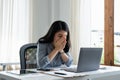 Tired business woman in stress works at a laptop while sitting at a table at home and holds her hand on her temples Royalty Free Stock Photo