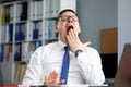Tired businessman office sits at table and yawns Royalty Free Stock Photo