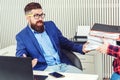 Tired businessman working with papers in office. Young bearded employee unhappy with excessive work