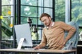 Tired businessman at workplace has severe back and lower back pain, young man working sitting at table with laptop and Royalty Free Stock Photo