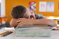 Tired caucasian schoolboy sitting at desk in classroom sleeping on a pile of schoolbooks Royalty Free Stock Photo