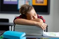 Tired caucasian schoolboy sitting at desk sleeping on pile of books in classroom Royalty Free Stock Photo