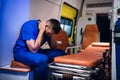 Tired corpsman in uniform sits inside the ambulance car and puts his hands on head