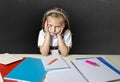 Tired cute junior schoolgirl with blond hair sitting in stress working doing homework looking bored