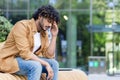 Tired and depressed young indian man sitting on a bench outside, smiling sad and holding his head Royalty Free Stock Photo