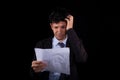 Tired and desperate businessman reading business document, isolated on black background. Young adult man worried about Royalty Free Stock Photo